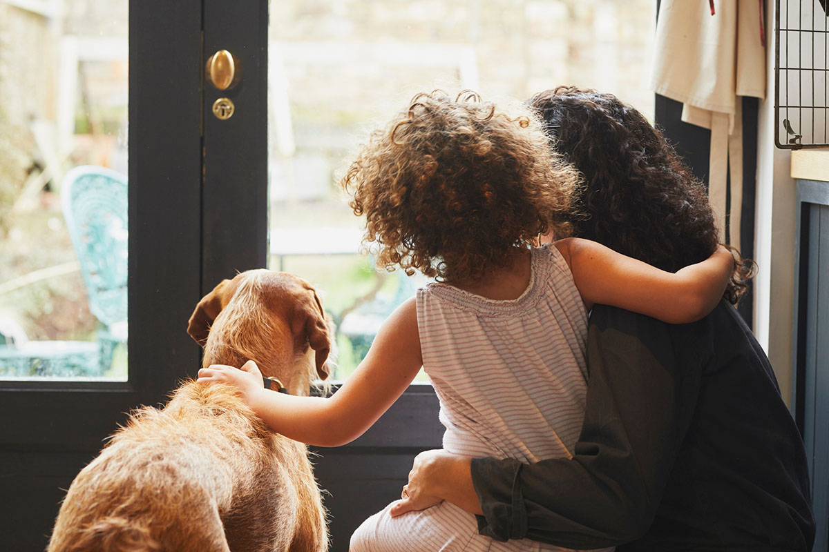 Mother, daughter and pet dog looking out the front door.